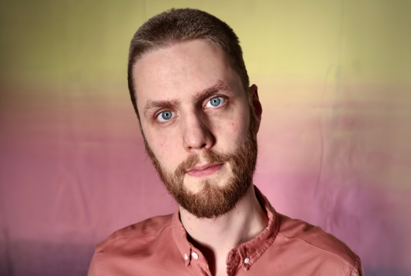 Dadi Freyr wearing an orange shirt and standing in front of a colourful backdrop.